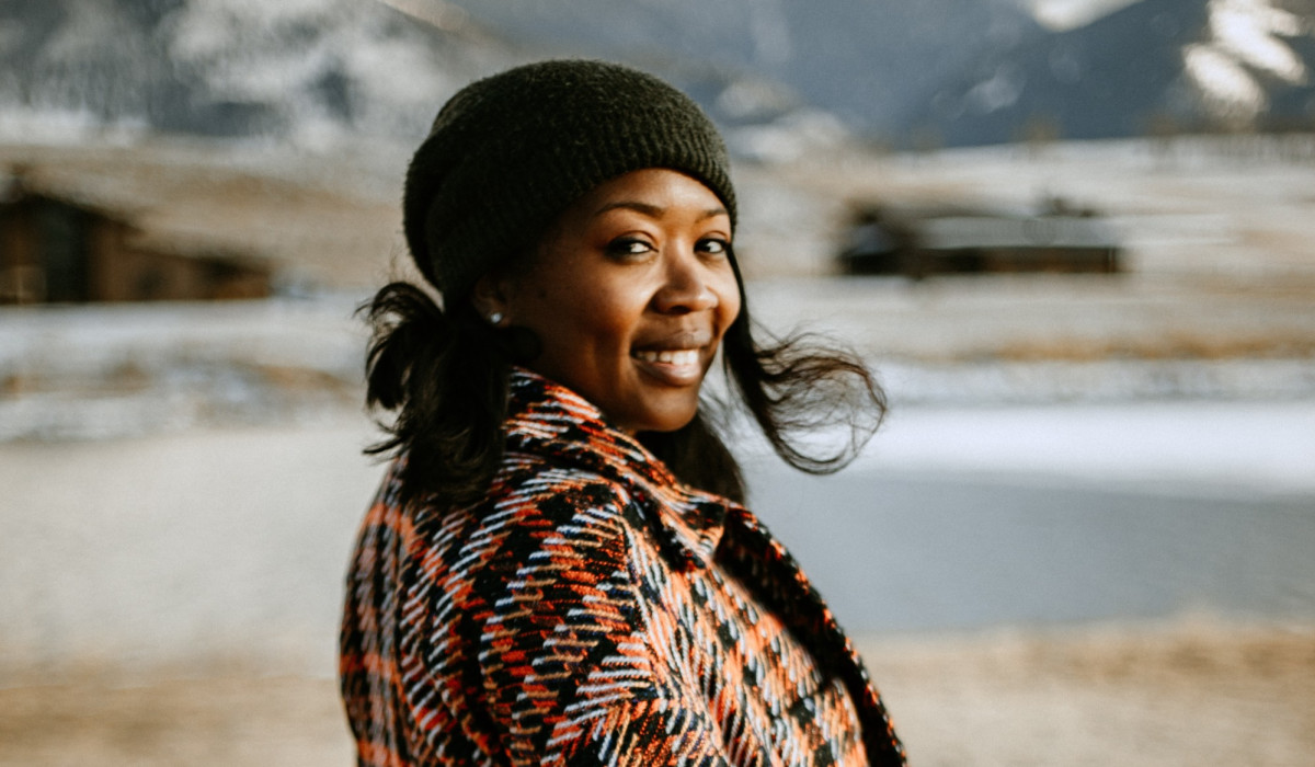Fora advisor Eunice in plaid winter jacket and beanie in front of snowy mountains. 