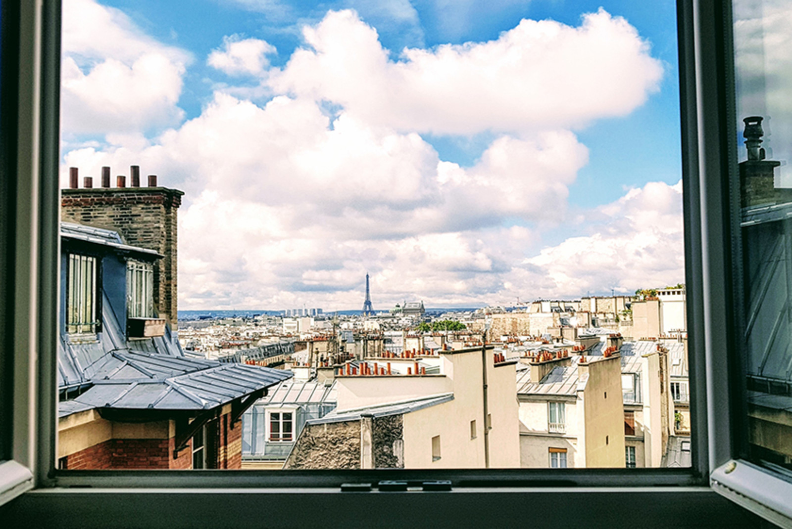 City view of Paris France out an open window with white clouds and blue sky and the Eiffel Tower in the distance