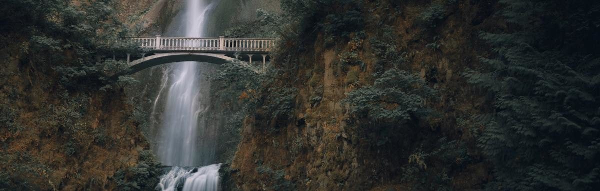 Waterfall at Columbia River Gorge in Oregon with bridge crossing over on a shady day.