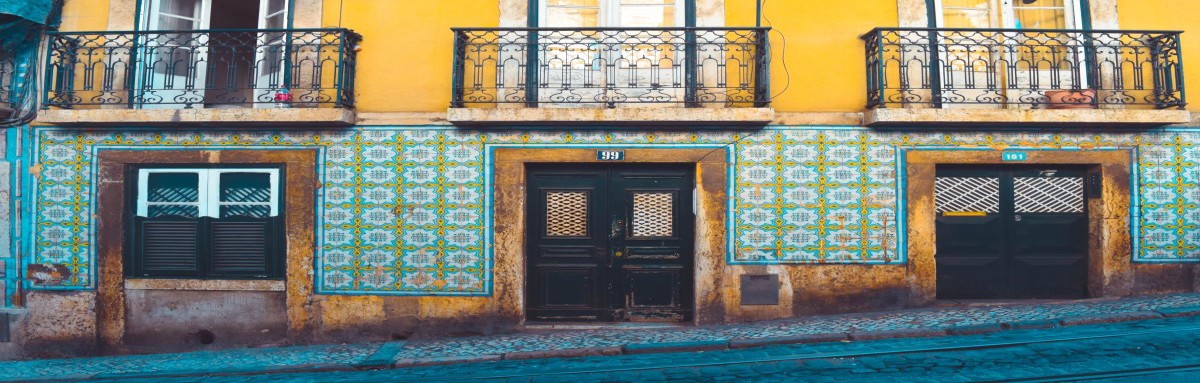 Building on a hilly street painted with bright colors and lined intricately-decorated tiles in Lisbon, Portugal.
