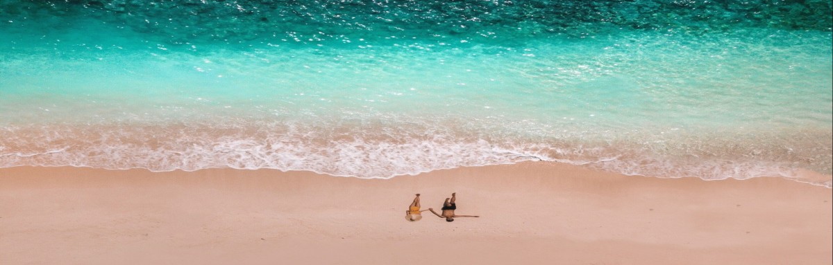 Couple holding hands and walking on a romantic private shore with turquoise ocean waters and white sands in the Bahamas.