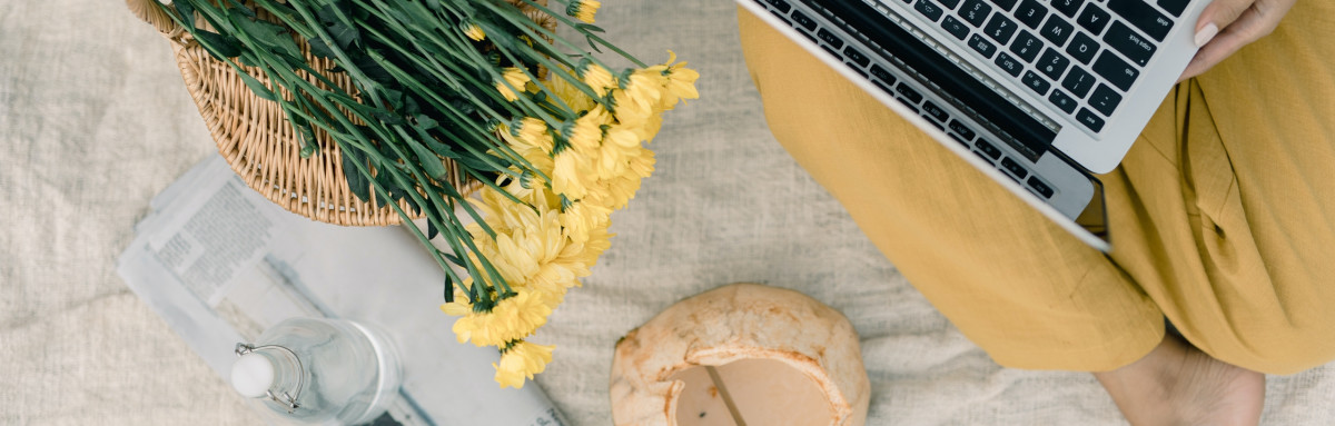 Woman using laptop next to yellow flowers in a photo taken from above