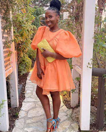 Fora Advisor Fallon Alexandria in orange puff dress and sky blue shoes in garden.