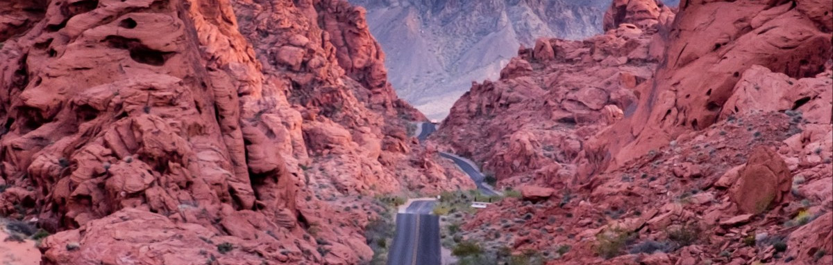 Open road stretching towards canyons of red rocks in Nevada. 