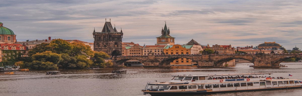 Charles Bridge over river in Prague before sunset with boat in water.