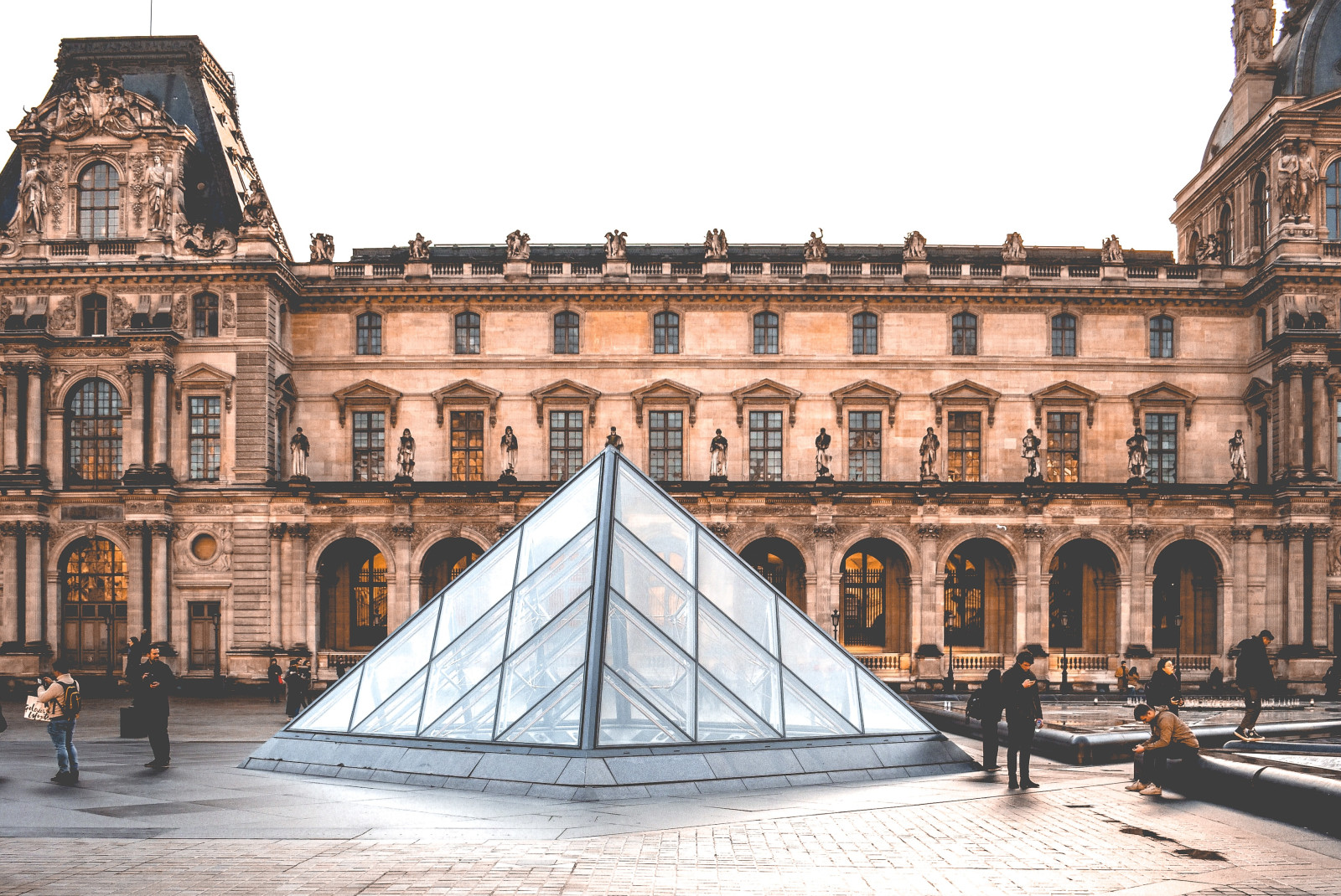 pink brown building louvre glass pyramid people standing outside