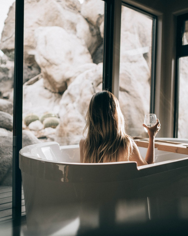 Woman with glass of wine in the tub looking at snow. 