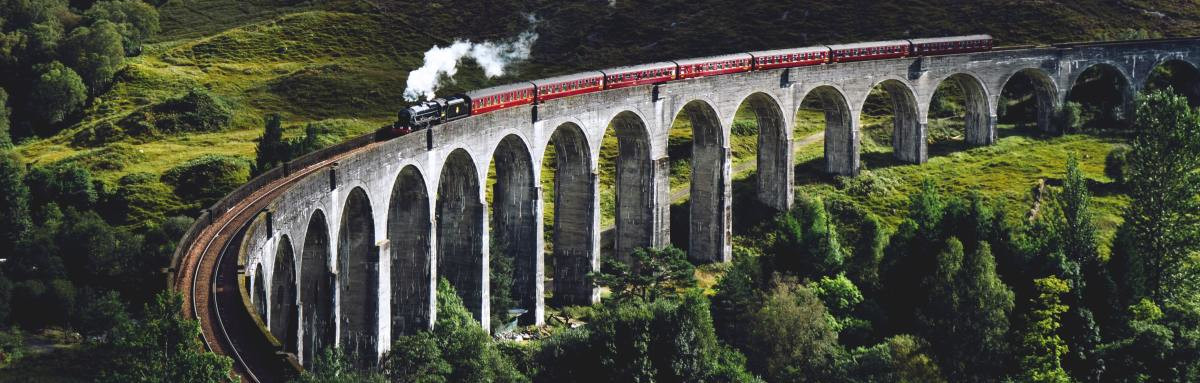 Train travels on bridge surrounded by lush green hills dotted with trees in Scotland 